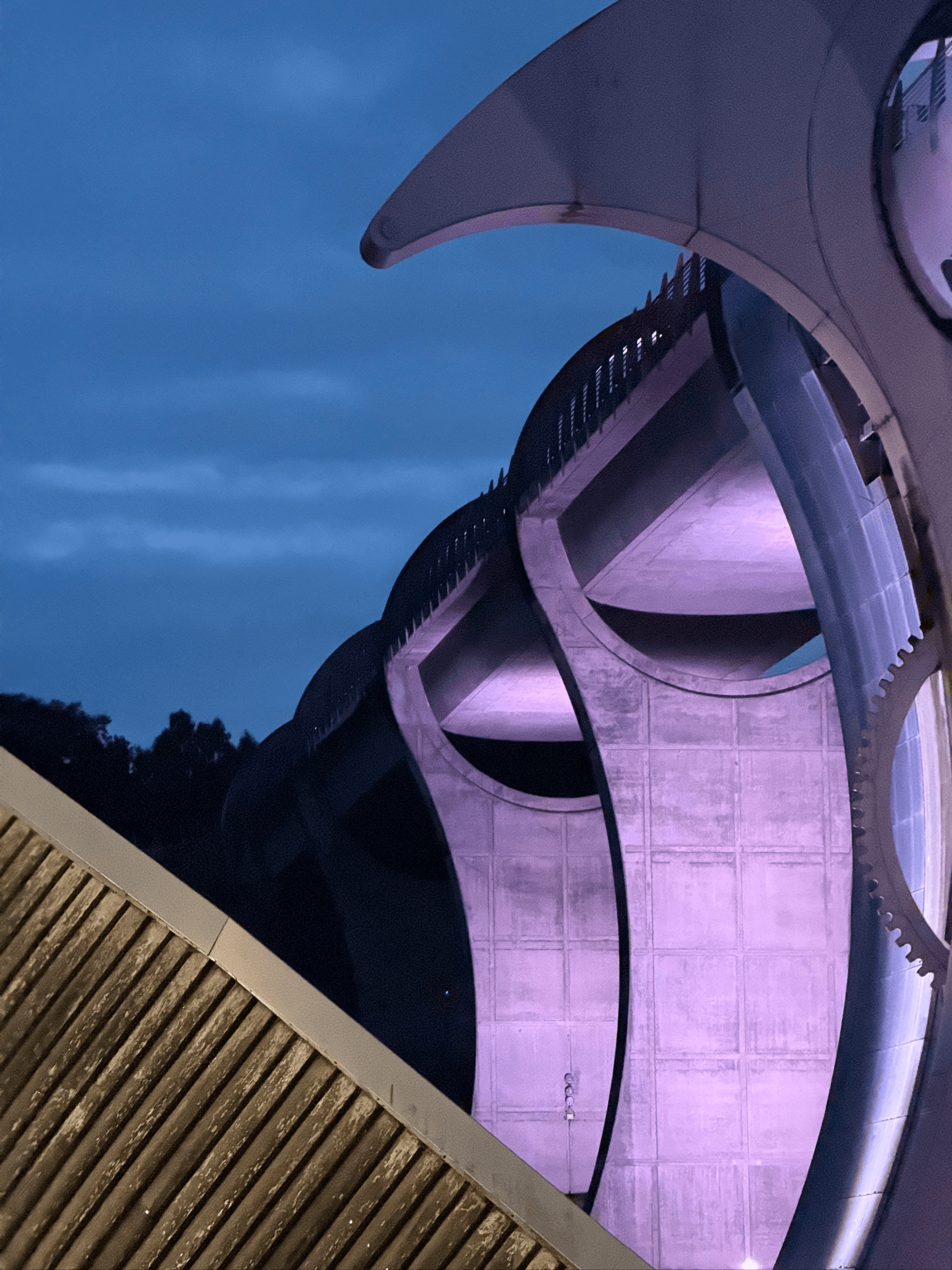 Abstract architectural structure with curving lines and purple lighting under a twilight sky.