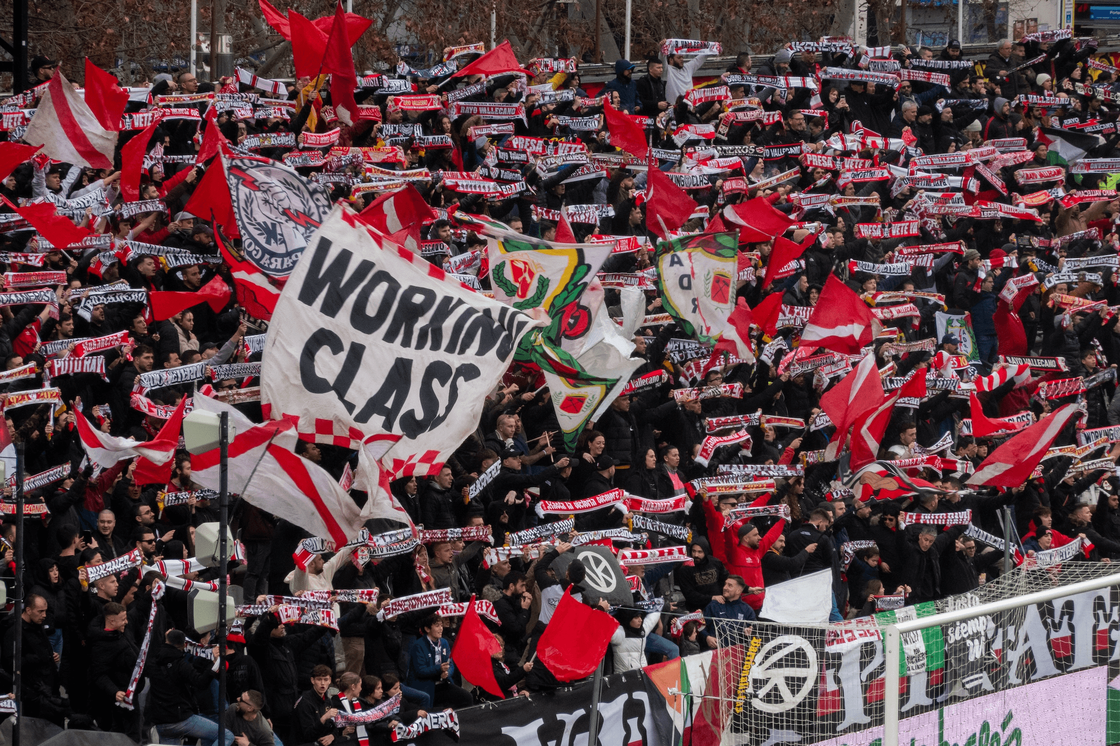 A large crowd of fans waving scarves and holding a banner reading "WORKING CLASS."