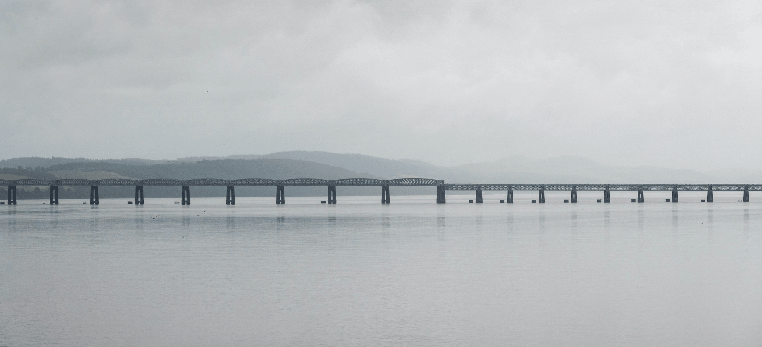 A long bridge spans a calm body of water under a cloudy sky.