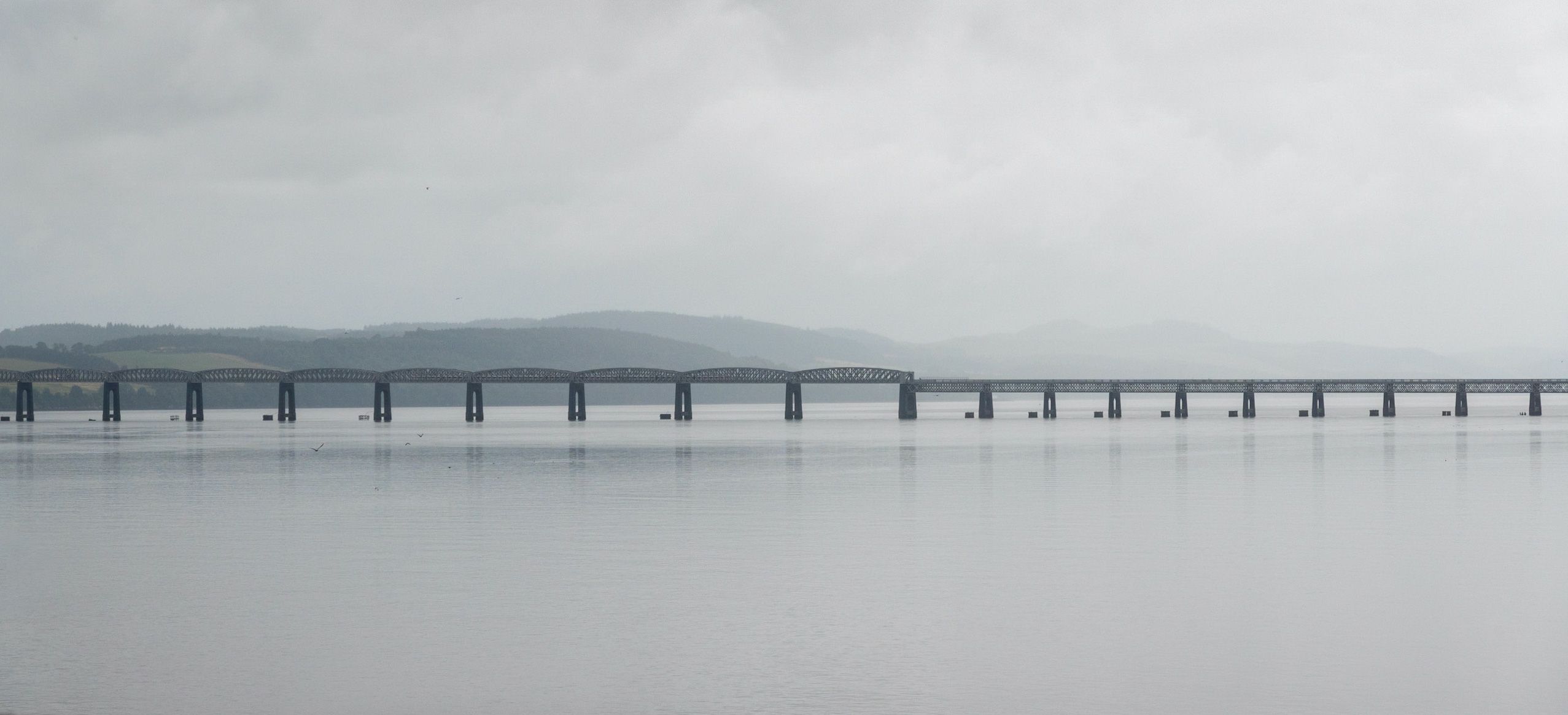 A long bridge spans a calm body of water under a cloudy sky.