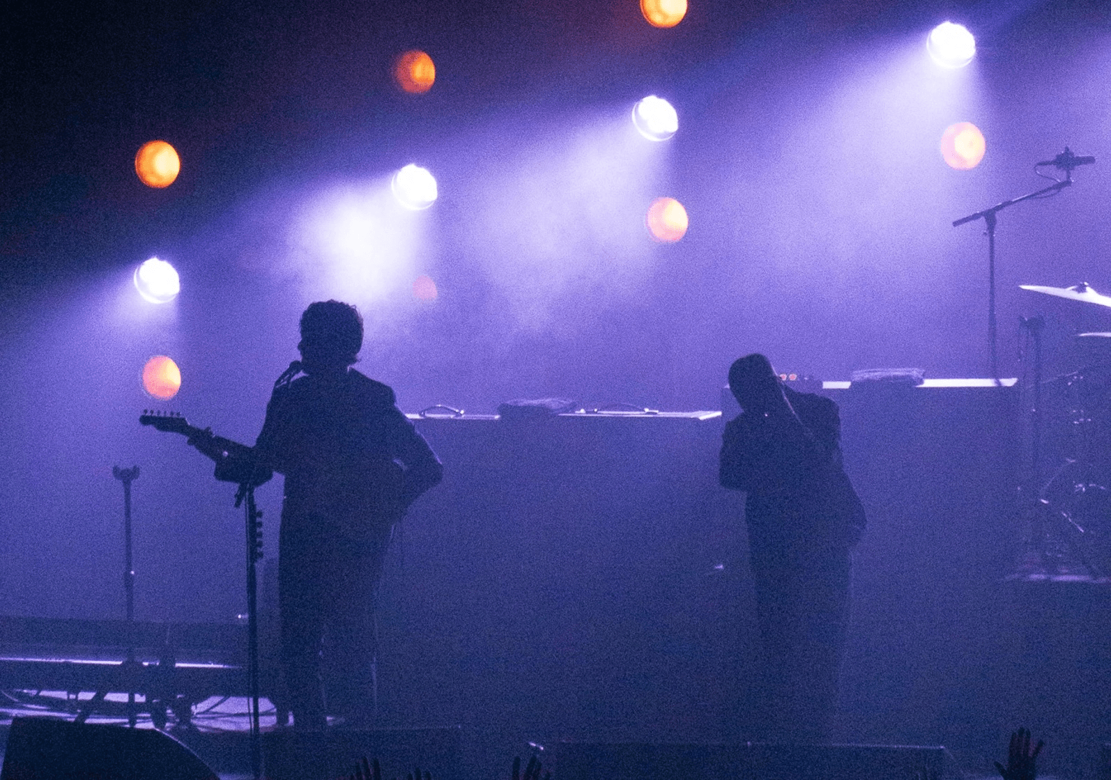 Silhouettes of two musicians performing on stage with dramatic lighting and smoke.