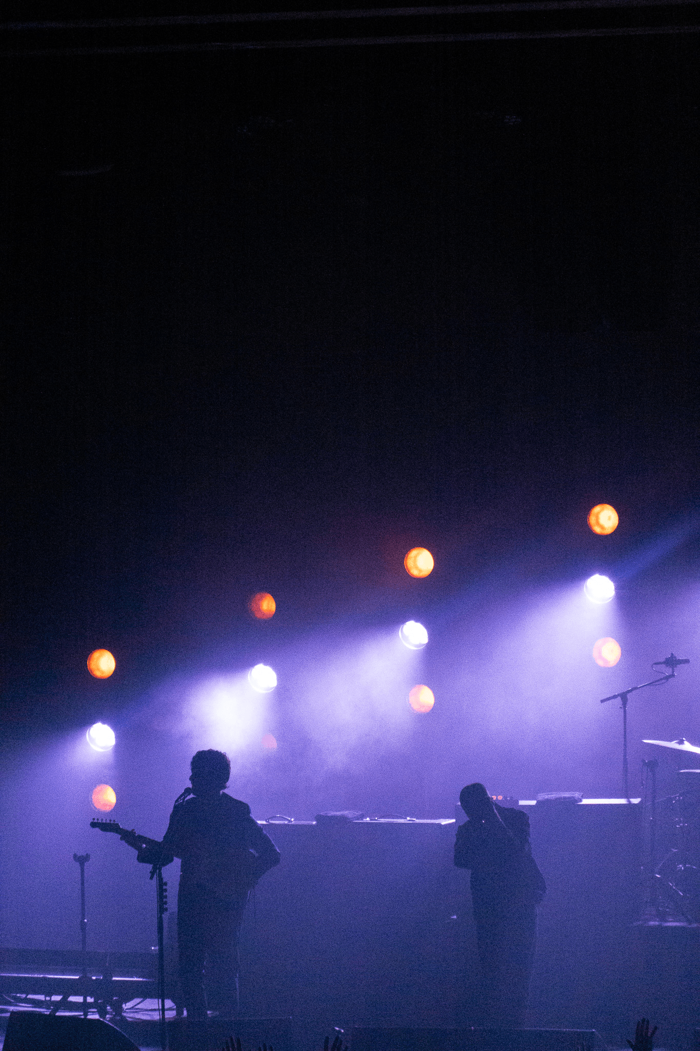 Silhouettes of two musicians on stage with purple spotlight and dim background.