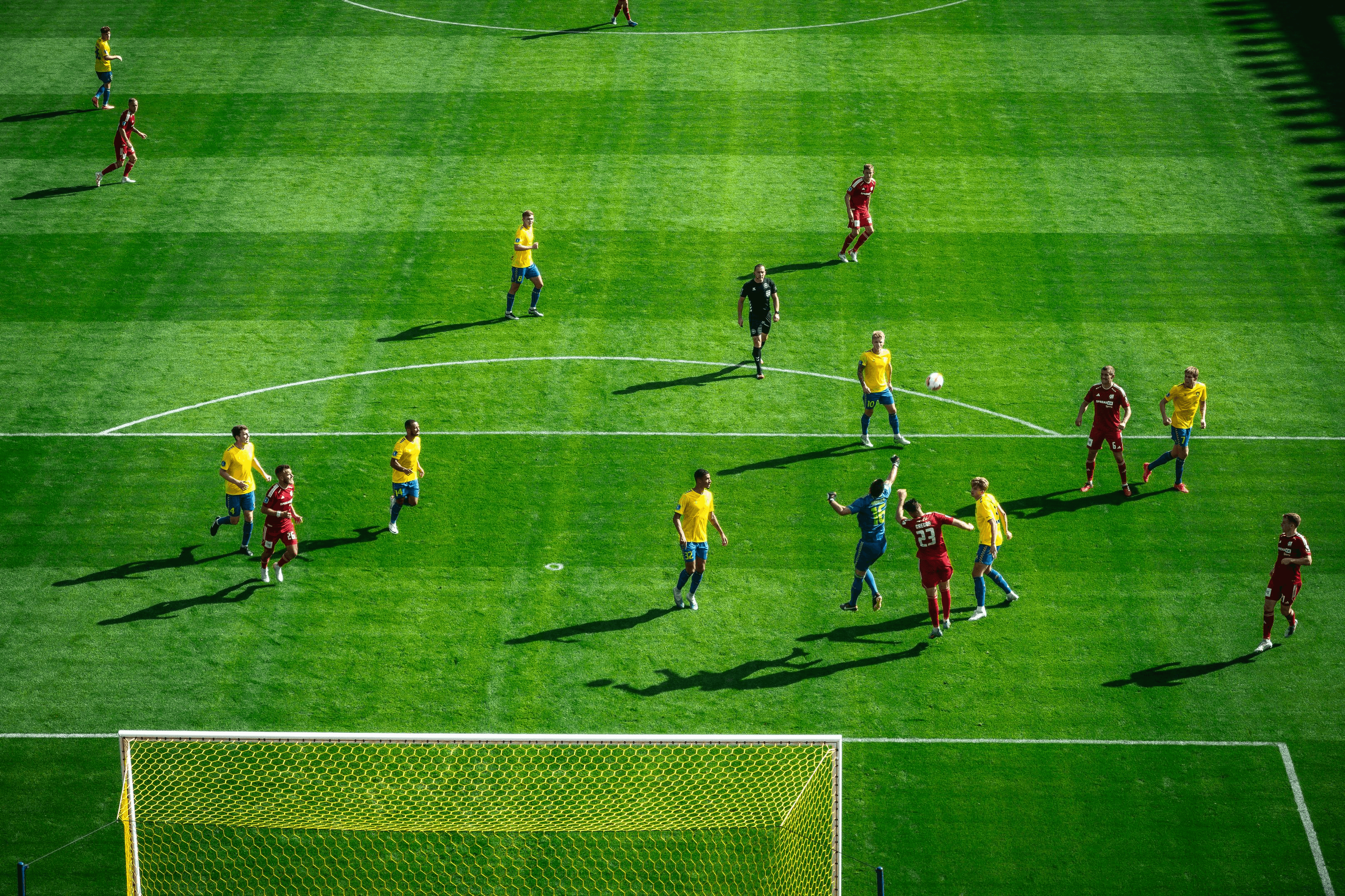 Aerial view of a soccer match with players in yellow and red jerseys on a green field.