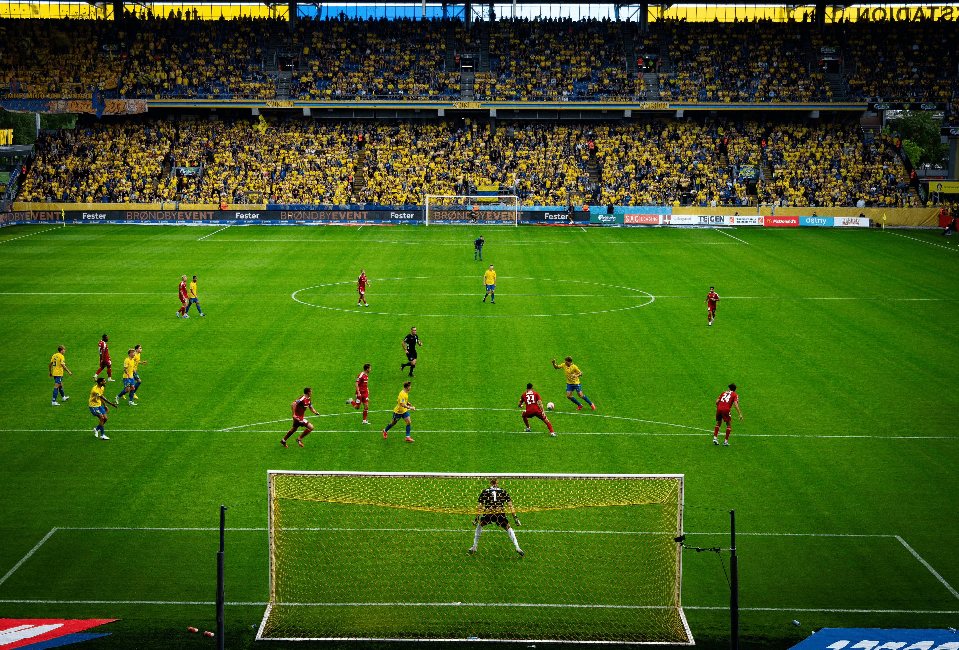 Soccer match in a stadium filled with fans; players on the field near the goal.