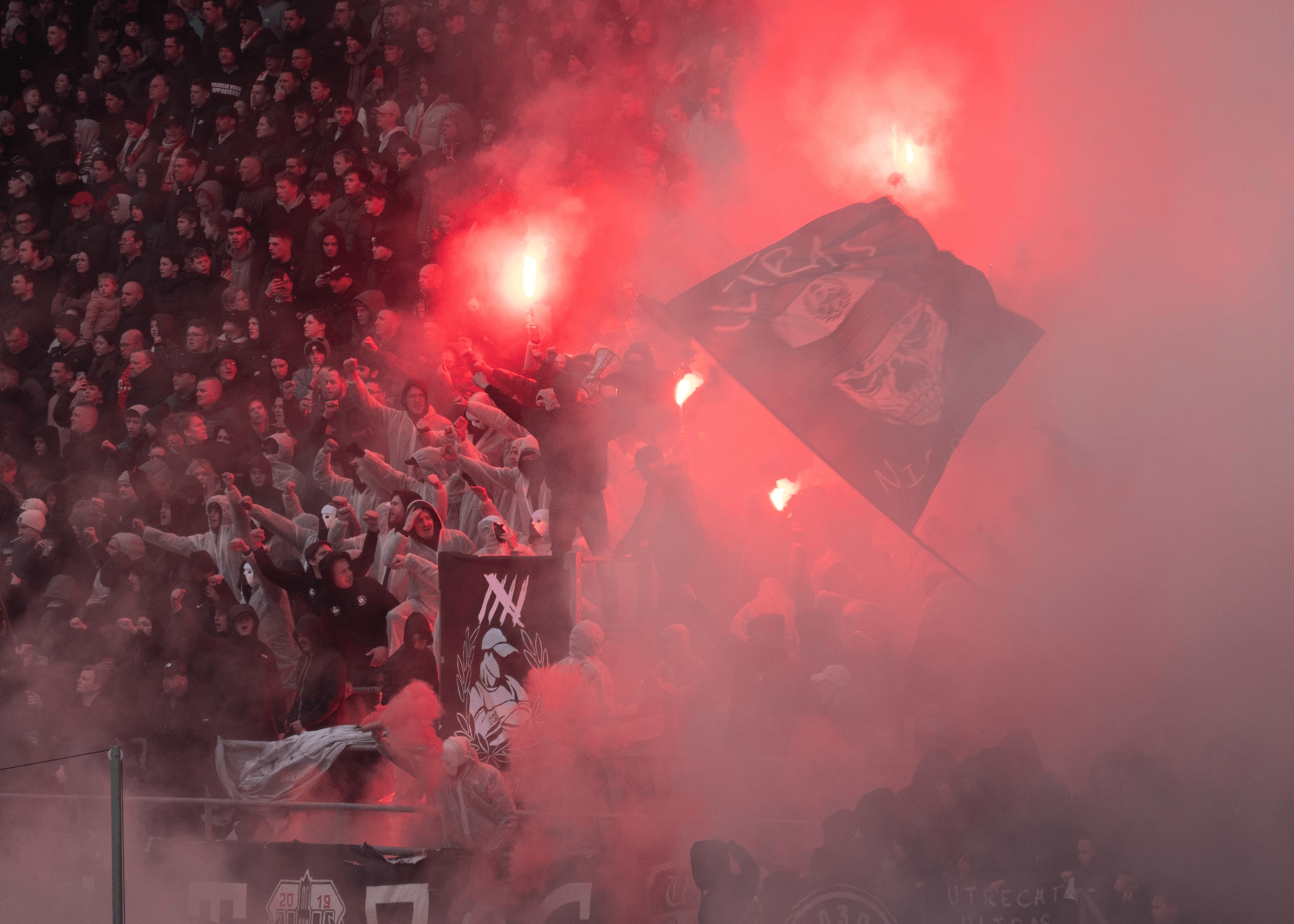 Crowd with flares and smoke at a sports event, waving flags and celebrating.